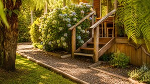 A wooden staircase leading to a wooden structure surrounded by lush greenery and flowering plants. - Top of the Otways the Country Cottage (Barramunga)