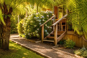 Una escalera de madera que conduce a una estructura de madera rodeada de exuberante follaje y plantas con flores.