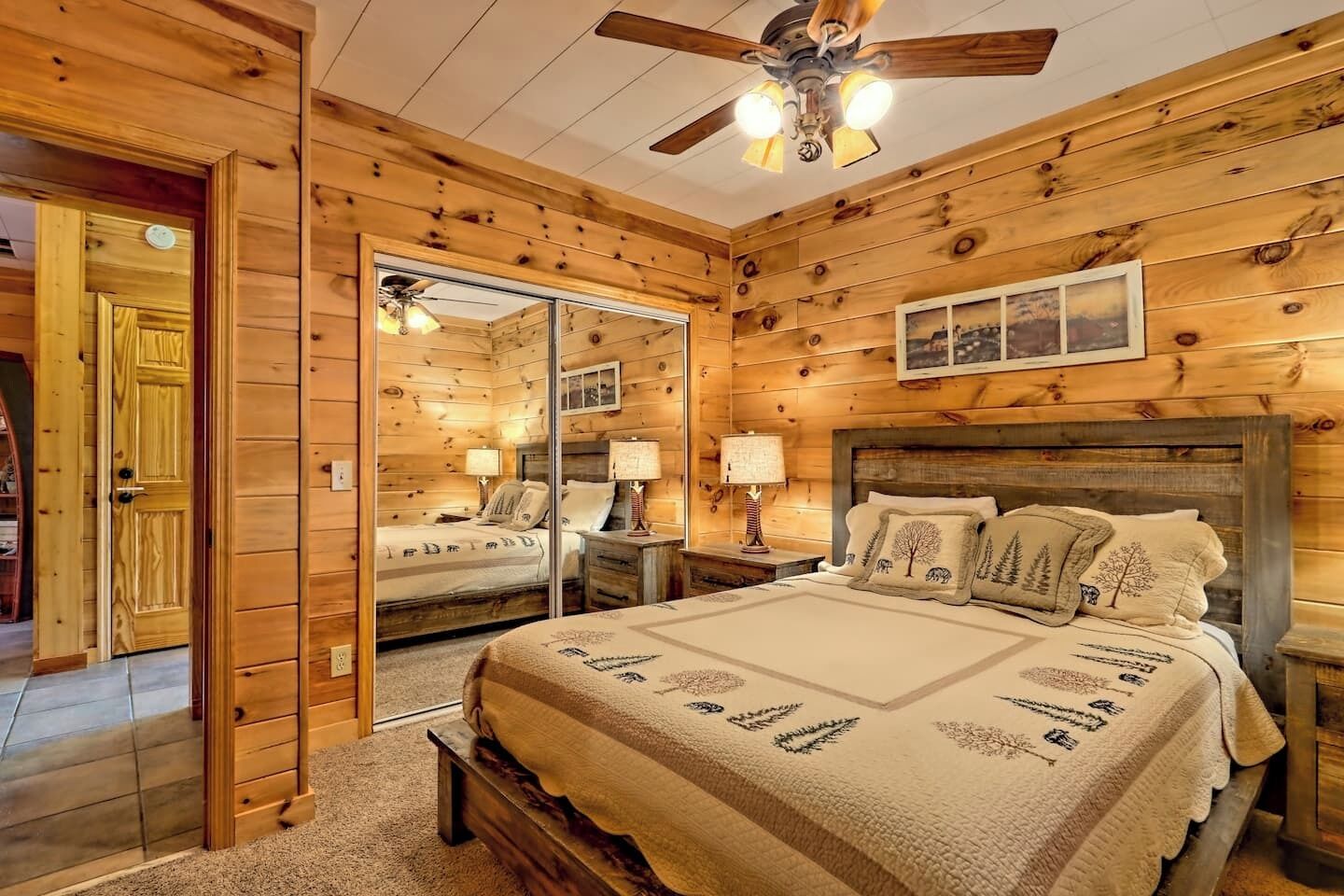 A wooden cabin bedroom with a bed, nightstands, a ceiling fan, and a mirror.
