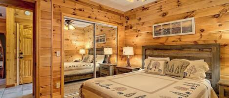 A wooden cabin bedroom with a bed, nightstands, a ceiling fan, and a mirror.