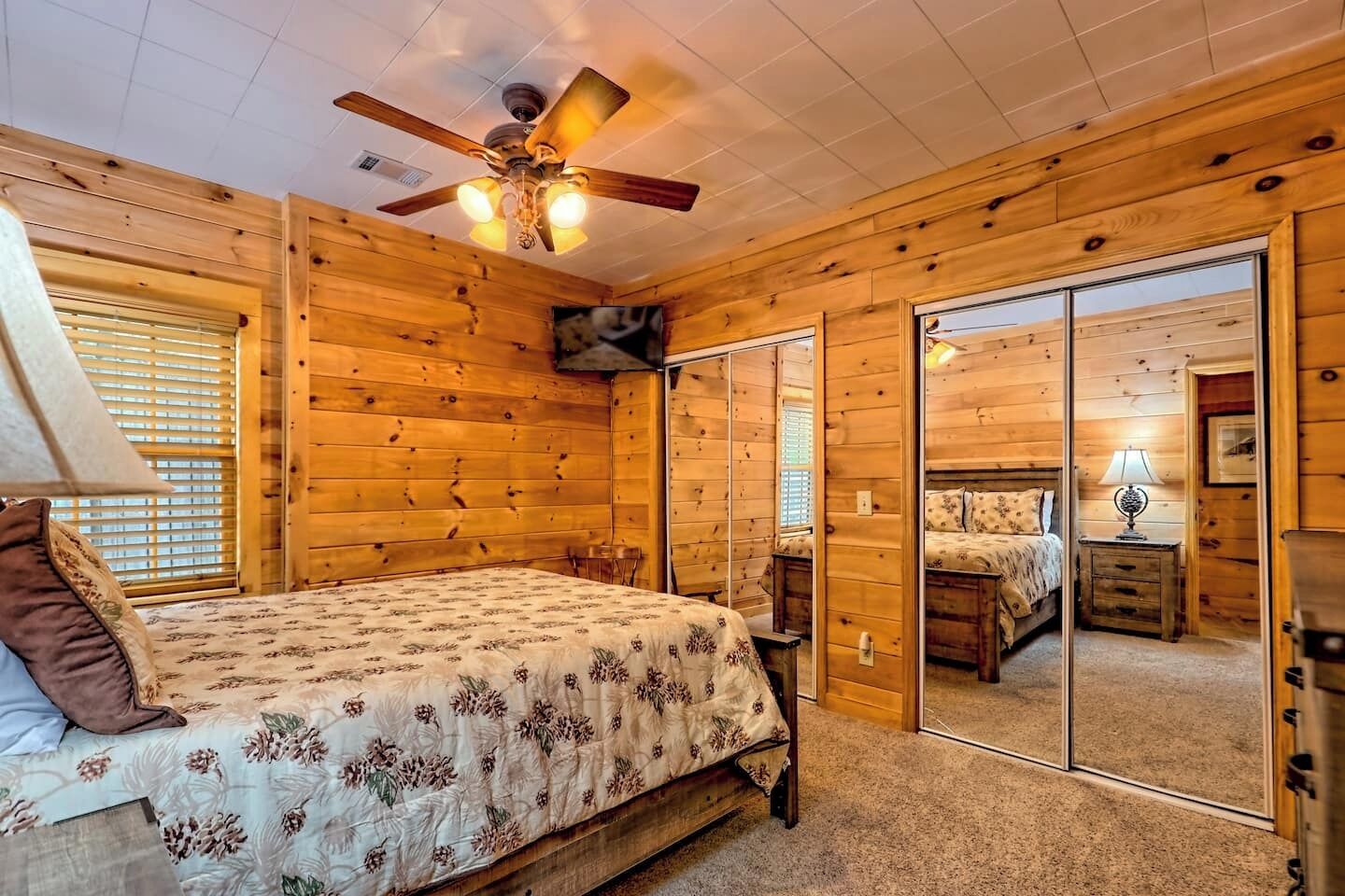 Ein Schlafzimmer einer Holzhütte mit einem Bett, einem Deckenventilator und einem großen Spiegel.