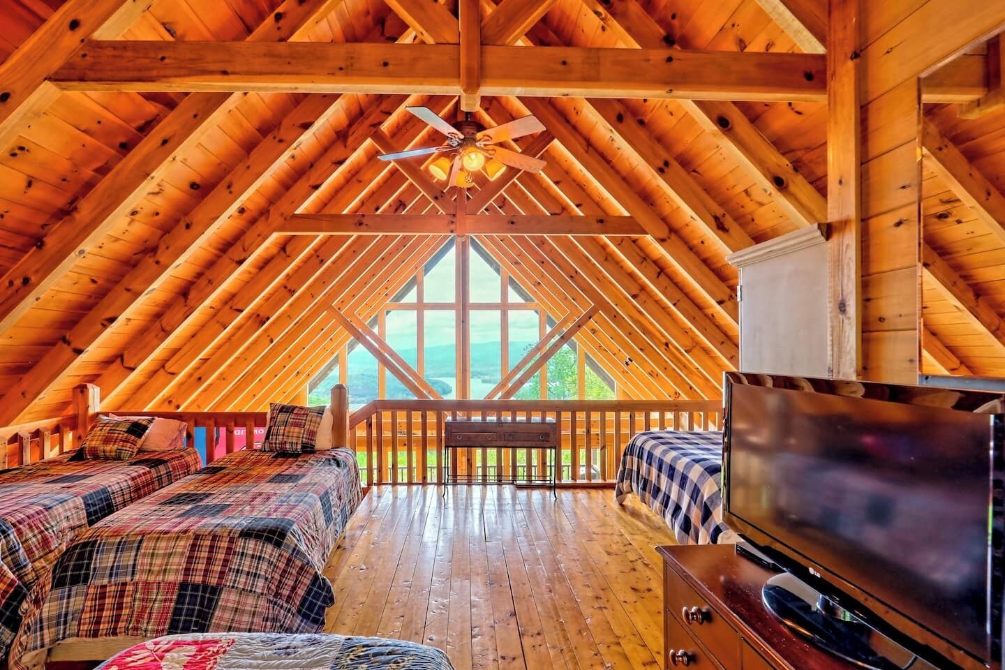 Une chambre spacieuse située dans les combles, avec une grande fenêtre, des poutres apparentes et un téléviseur.