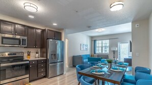 Una cocina moderna con armarios oscuros, electrodomésticos de acero inoxidable y un comedor con sillas azules y una mesa de madera.
