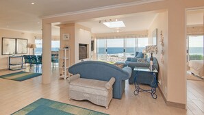 A spacious living area with a view of the sea, a sofa, a small table, and a wicker chair.