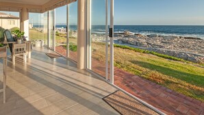 A modern room with large glass doors leading to a patio with a view of the rocky coastline. - HERMANUS Haven, entire home with private pool, on the sea (Hermanus)