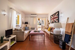 A living room with a sofa, a coffee table, a TV on a stand, a lamp, and a flag on the wall.
