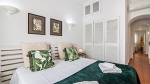 Habitación de hotel con cama, almohadas, manta verde, mesita de noche y lámpara fijada a la pared.