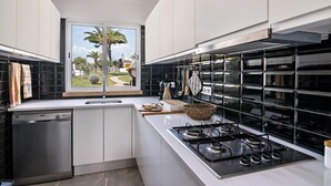 Una cocina moderna con armarios blancos, un salpicadero de azulejos negros, una estufa a gas y un lavavajillas.