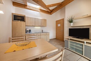 Une cuisine compacte avec des meubles en bois, un four à micro-ondes, une machine à café et un téléviseur posé sur un meuble en bois.