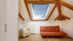 Una habitación con techo inclinado, tragaluz, radiador blanco, silla blanca y sofá naranja.