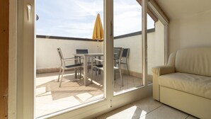 Una habitación con puerta corrediza de vidrio que da a un patio exterior con mesa y sillas, y un sofá en el interior.