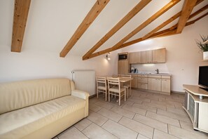 Un salon moderne avec un canapé, des poutres en bois, un coin repas et une cuisine dotée de meubles en bois et d’un téléviseur.
