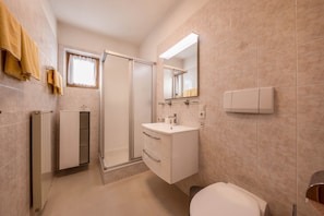 A bathroom with a toilet, sink, mirror, towel rack, and shower.