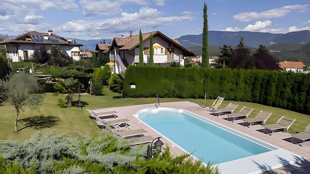 A swimming pool with lounge chairs, surrounded by well-maintained greenery and a view of houses and mountains. - Apartment "Stompferhof Family" in Caldaro with Shared Pool & Garden (Kaltern)
