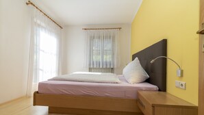 A bedroom with a bed, bedside table, lamp, and a window with curtains. - Apartment "Stompferhof Family" in Caldaro with Shared Pool & Garden (Kaltern)