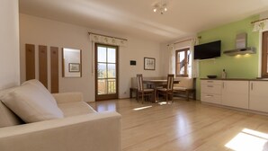 A living room with a sofa, dining table, chairs, and a kitchen area with cabinets and a TV. - Apartment "Stompferhof Family" in Caldaro with Shared Pool & Garden (Kaltern)