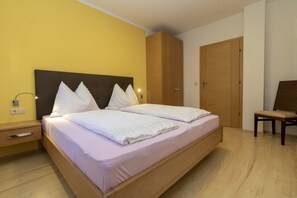 A double bed with a headboard, a bedside table, a lamp, and a wooden wardrobe.