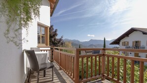 A wooden deck with a chair and table, overlooking a mountainous landscape. - Apartment "Stompferhof Family" in Caldaro with Shared Pool & Garden (Kaltern)