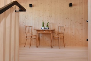A wooden room with two chairs and a small table, a wooden wall, and a black object on the wall.