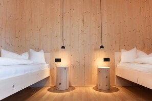 Une chambre avec deux lits, un plancher en bois et des luminaires suspendus.