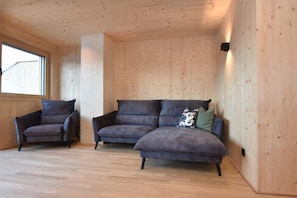A room with wooden walls and floors, a window, a sofa, and a chair.