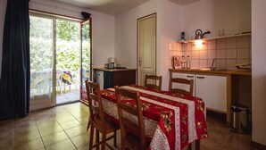 A dining area with a table set for four, a kitchen area with a sink and cabinets, and a sliding glass door leading to an outdoor area. - Cottage in Vézac near Forest and Lake (Vezac)