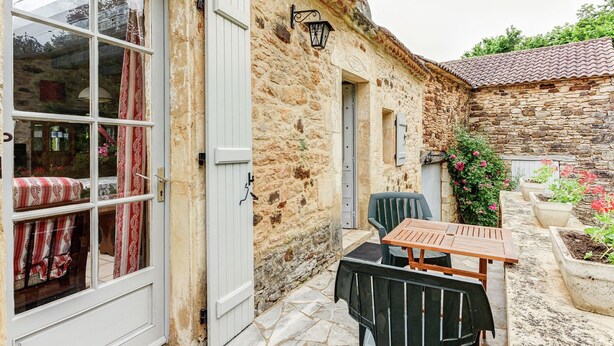 A stone building with a wooden door, a small table, and chairs outside. - Holiday home  with garden (Villefranche-Du-Périgord)