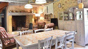 A rustic dining area with a wooden table and chairs, a fireplace, and a stone wall. - Holiday home  with garden (Villefranche-Du-Périgord)