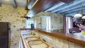 A rustic kitchen with a stone wall, wooden beams, a sink, and a refrigerator. - Holiday home  with garden (Villefranche-Du-Périgord)