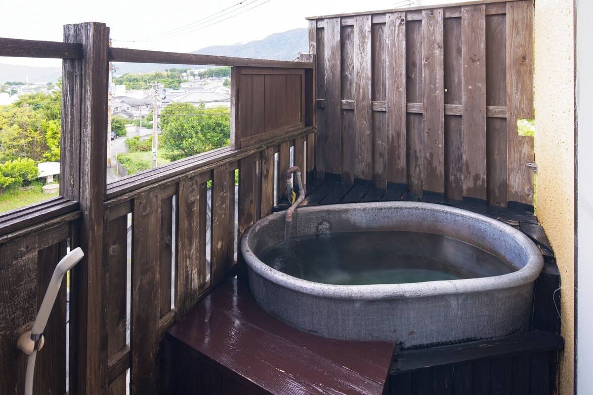A wooden balcony with a hot tub, a view of a town, and a mountain in the background.