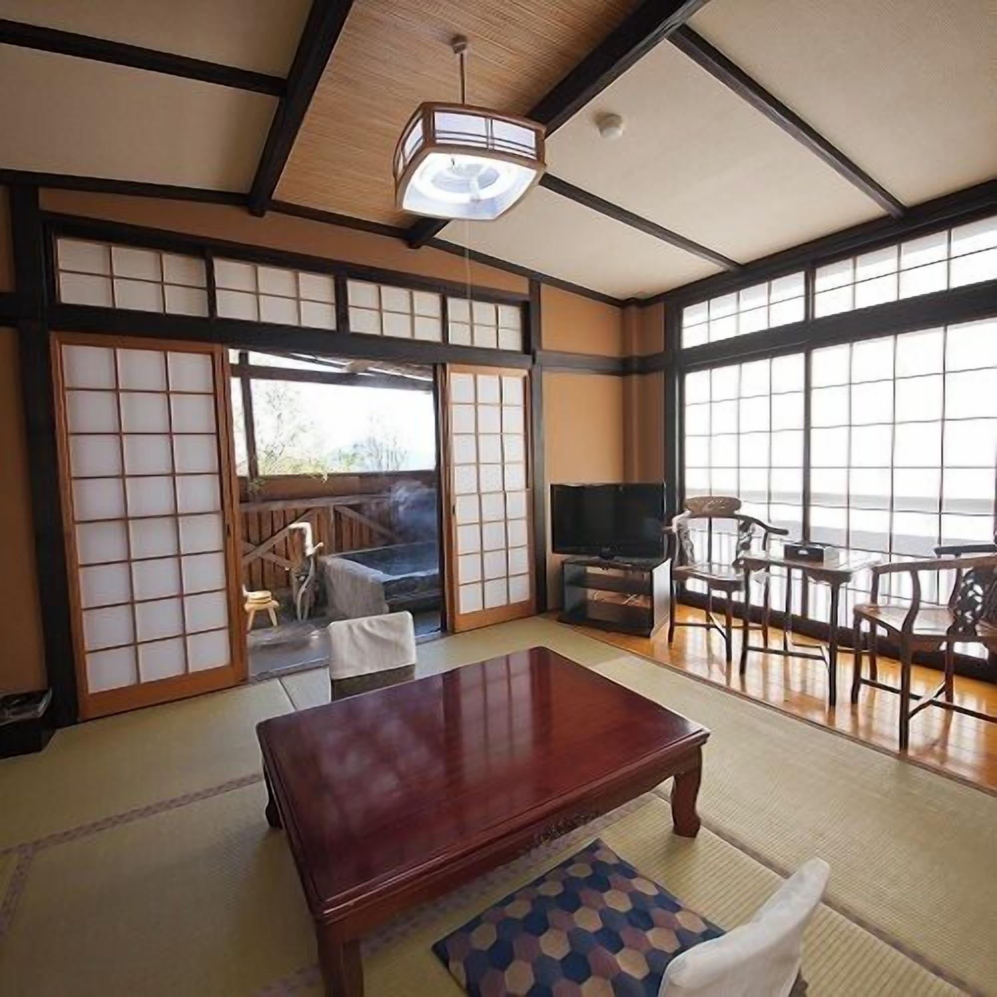 Ein traditioneller japanischer Raum mit Tatami-Boden, einem niedrigen Holztisch, einem Fernseher und Schiebetüren.