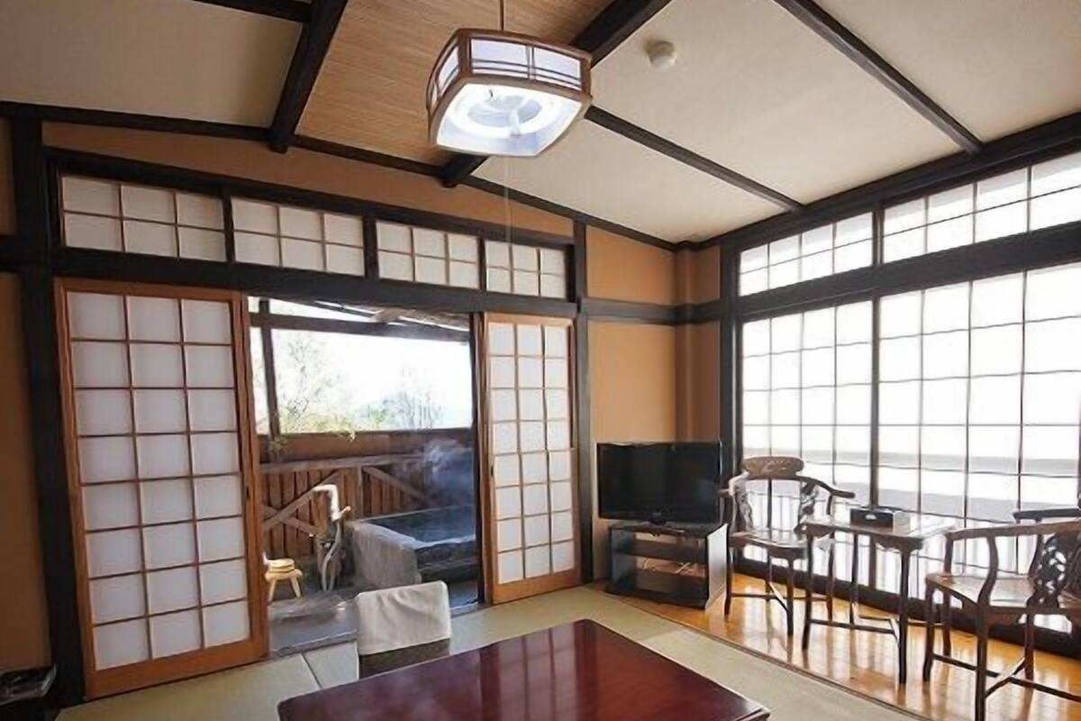 A traditional Japanese room with tatami flooring, a low wooden table, a TV, and sliding doors.