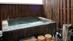 A stone hot tub with wooden walls and a wooden deck outside.