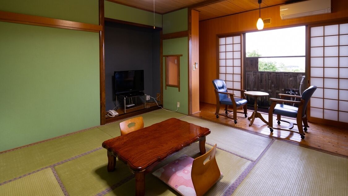 A tatami mat room with a wooden table, chairs, a television, and a sliding door.