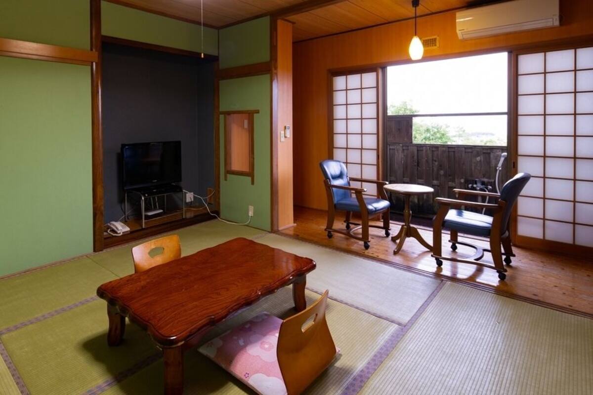 A tatami mat room with a wooden table, chairs, a television, and a sliding door.