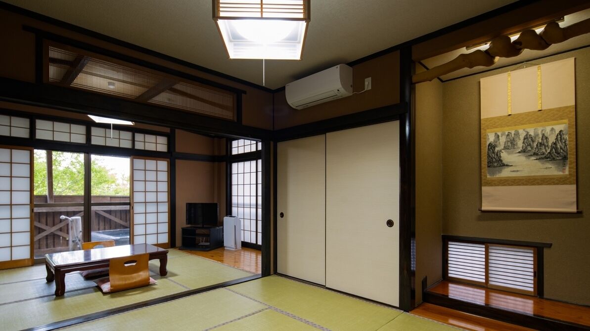 A traditional Japanese room with tatami flooring, sliding doors, a tatami mat table, a television, and artwork on the walls.