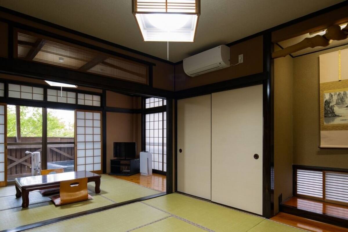 A traditional Japanese room with tatami flooring, sliding doors, a tatami mat table, a television, and artwork on the walls.