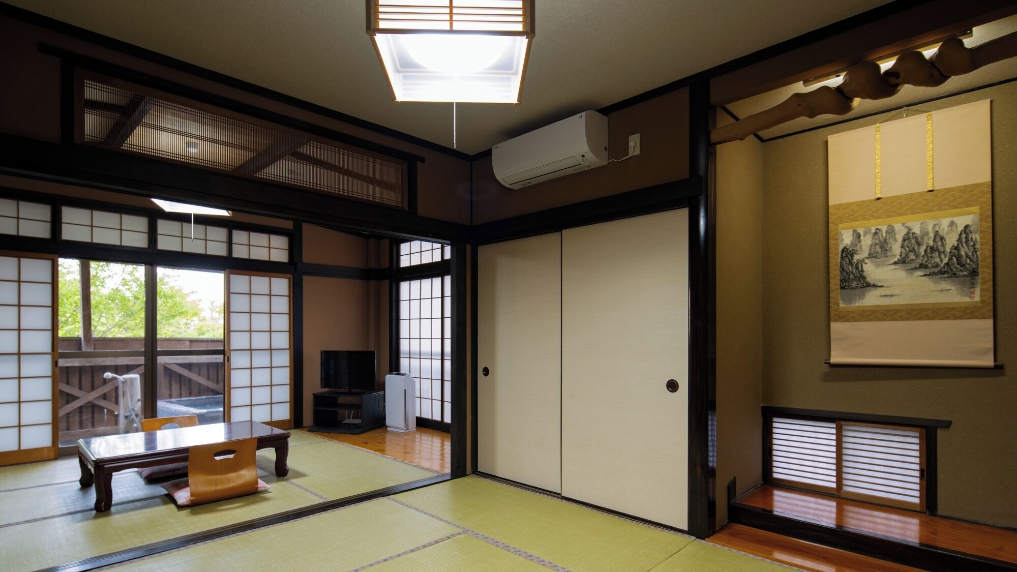 Ein traditioneller japanischer Raum mit Tatami-Böden, Schiebetüren, einem Fernseher und einem Gemälde an der Wand.