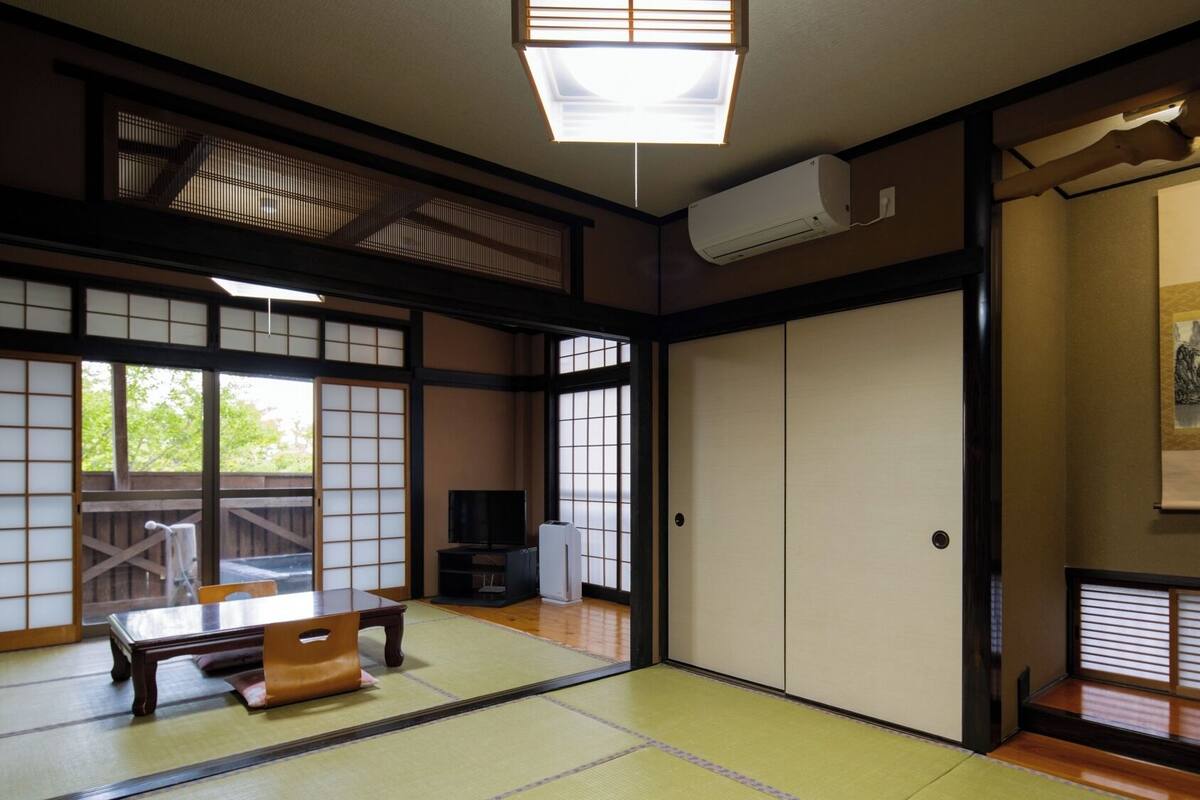 A traditional Japanese room with tatami flooring, sliding doors, a television, and a painting on the wall.
