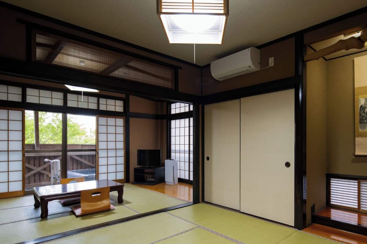 A traditional Japanese room with tatami flooring, sliding doors, a television, and a painting on the wall.
