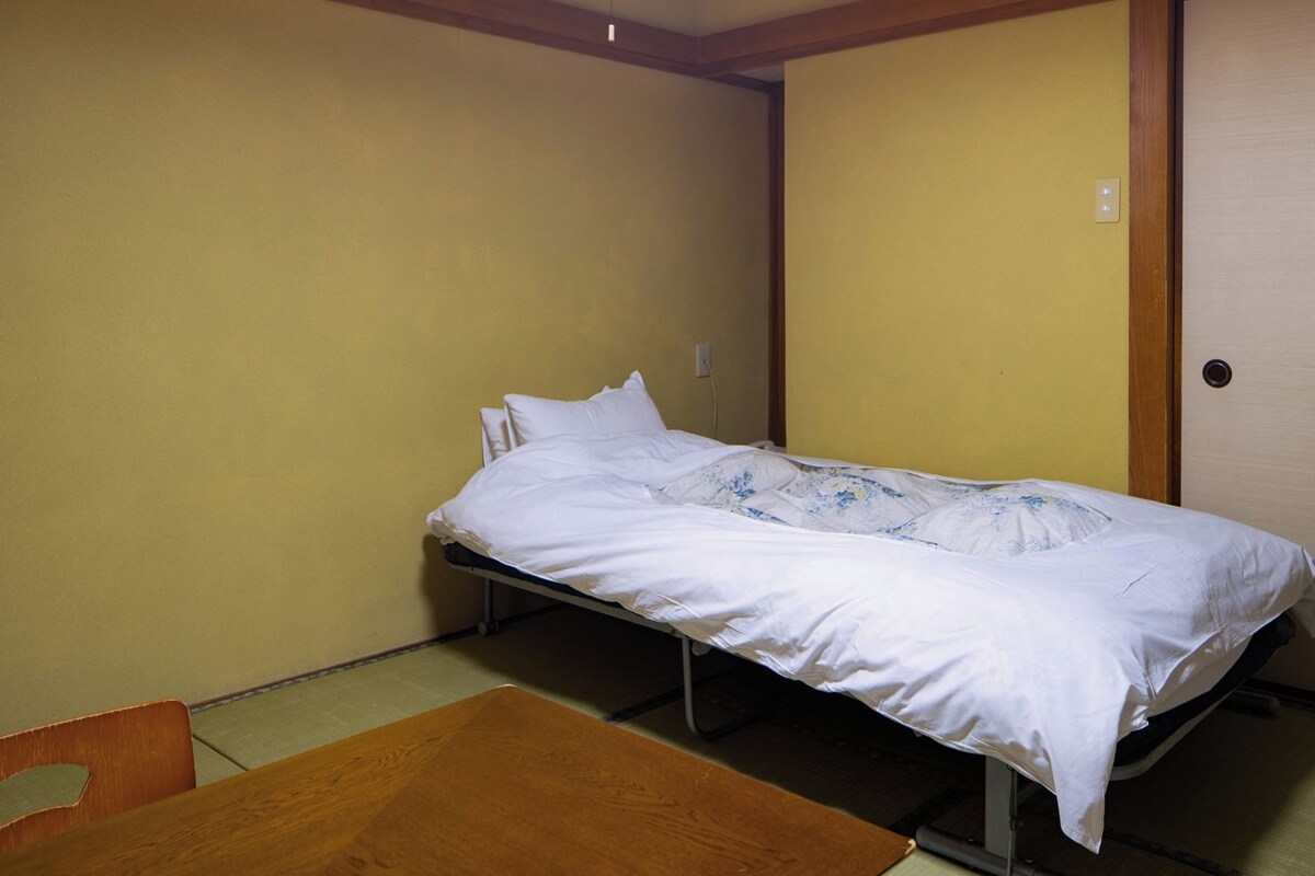 A single bed with white bedding in a room with yellow walls and a wooden floor.