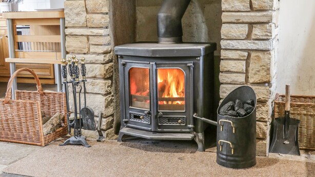 A stone fireplace with a wood-burning stove, surrounded by wicker baskets and a metal bucket. - The Smithy (Richmond)