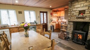 A cozy kitchen with wooden cabinets, a stone fireplace, and a dining area with a wooden table and chairs. - The Smithy (Richmond)