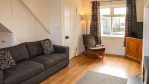 A living room with a sofa, armchair, wooden cabinet, and a television. - Rosies Cottage (Bushmills)
