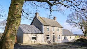 A two-story house with a gravel driveway and a lawn. - Rosies Cottage (Bushmills)