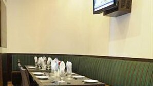 A conference room with a long table, chairs, a bench, a flat-screen TV, and a wall-mounted air conditioning unit. - Pallavi Ávida (Panvel)