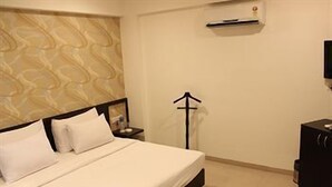 A hotel room with a bed, a nightstand, a TV, and a wall-mounted air conditioner. - Pallavi Ávida (Panvel)