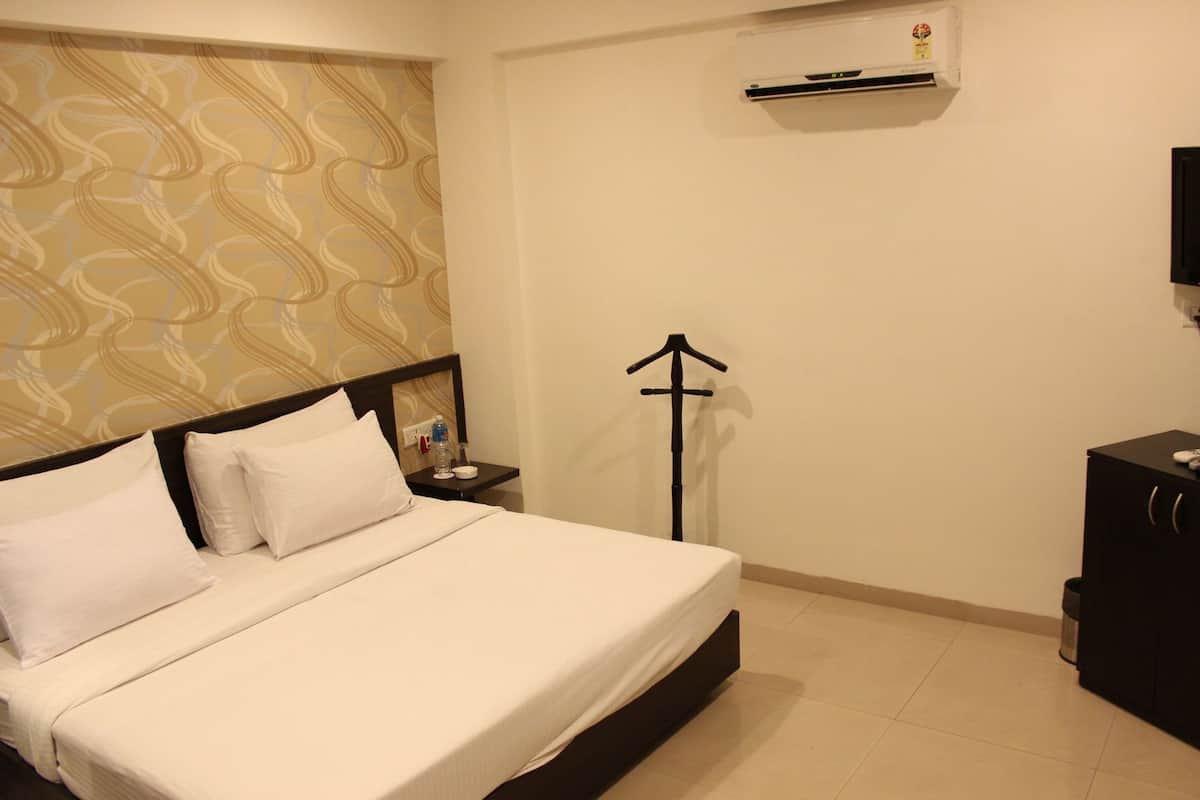 A hotel room with a bed, a nightstand, a water bottle, a black coat rack, and a TV on the wall.