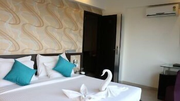 A hotel room with a bed, a swan-shaped pillow, and a patterned headboard. - Pallavi Ávida (Panvel)