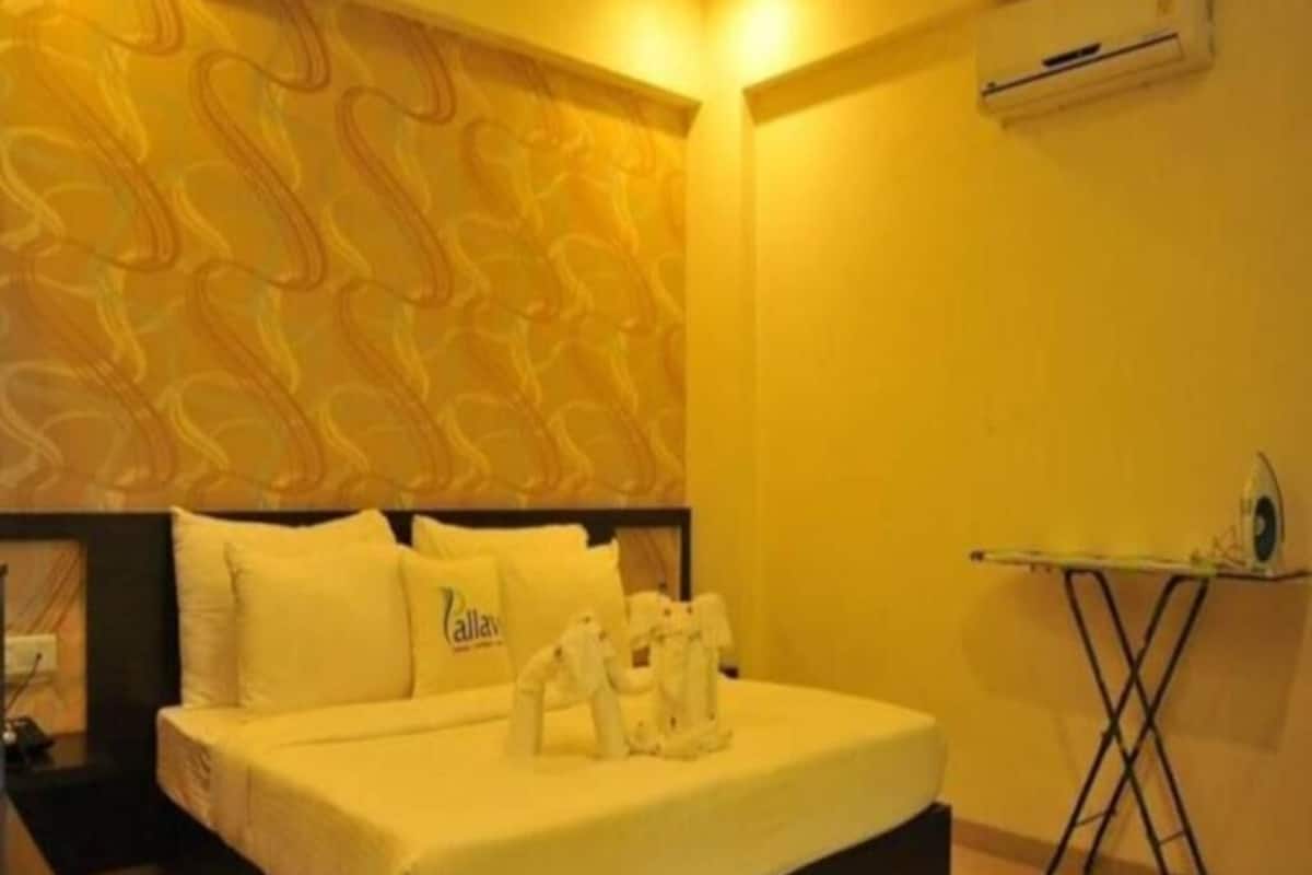 A hotel room with a bed, a nightstand, a wall-mounted air conditioner, and a small table with a fan.